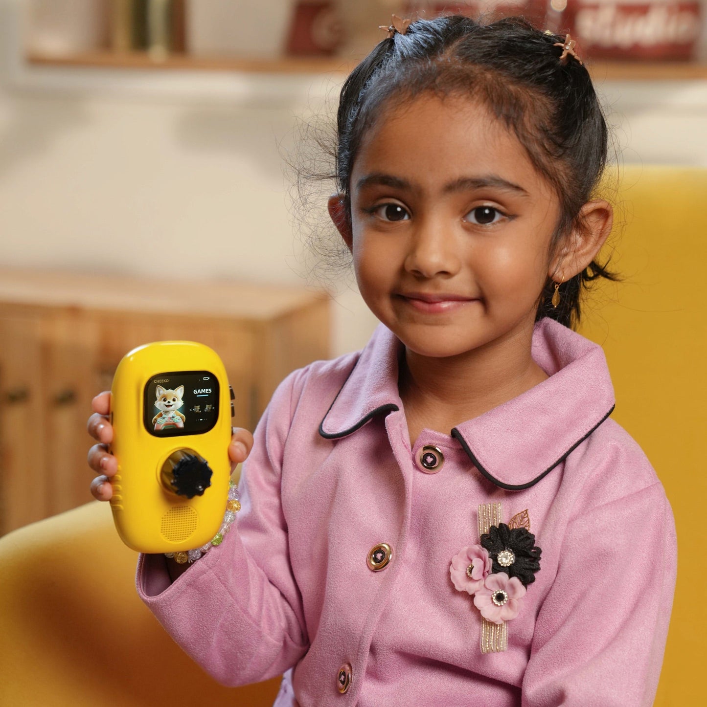 A young girl smiling and holding a yellow Cheeko showing the Games screen
